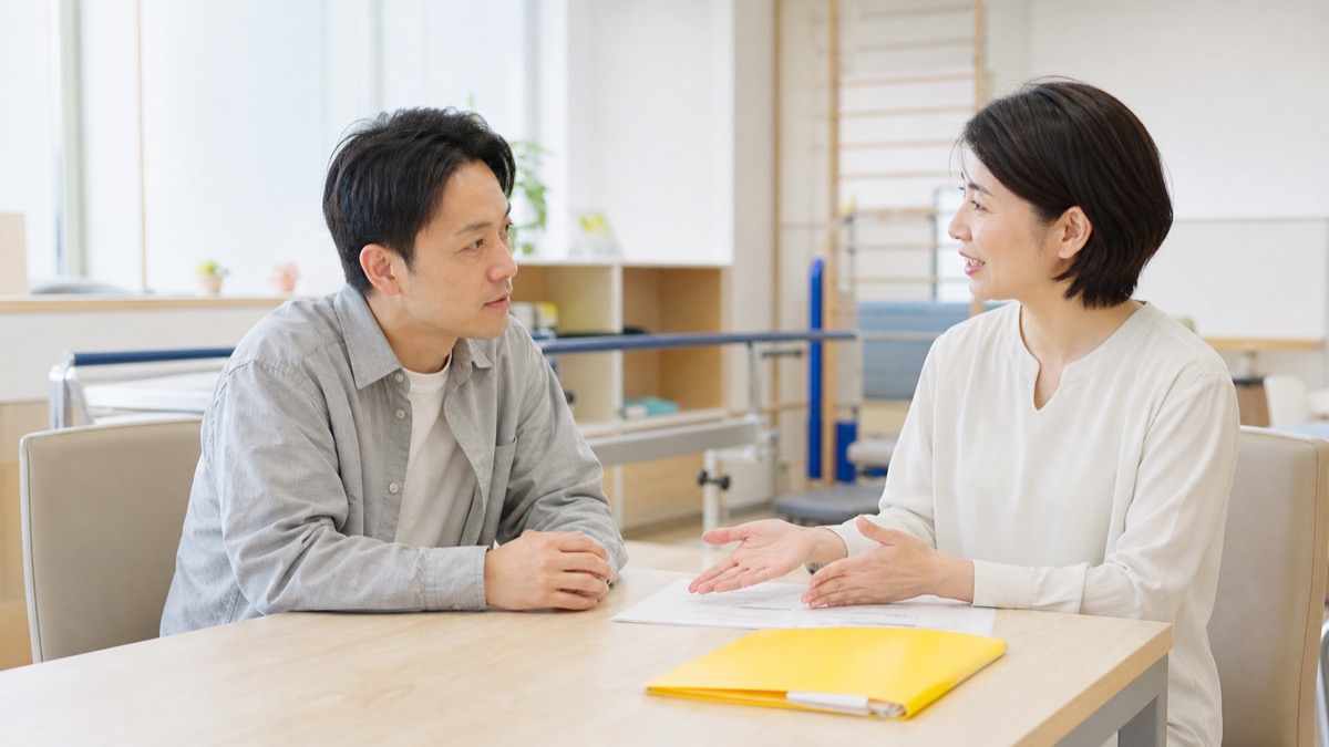 30代社会人と教員が明るい相談室で社会人入試の選択肢について話し合っているシーン